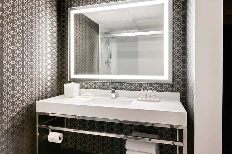 Contemporary bathroom with geometric patterned wallpaper, illuminated mirror, and white sink