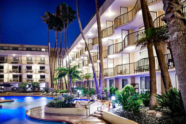 Nighttime view of illuminated hotel building with palm trees and lit blue pool in courtyard