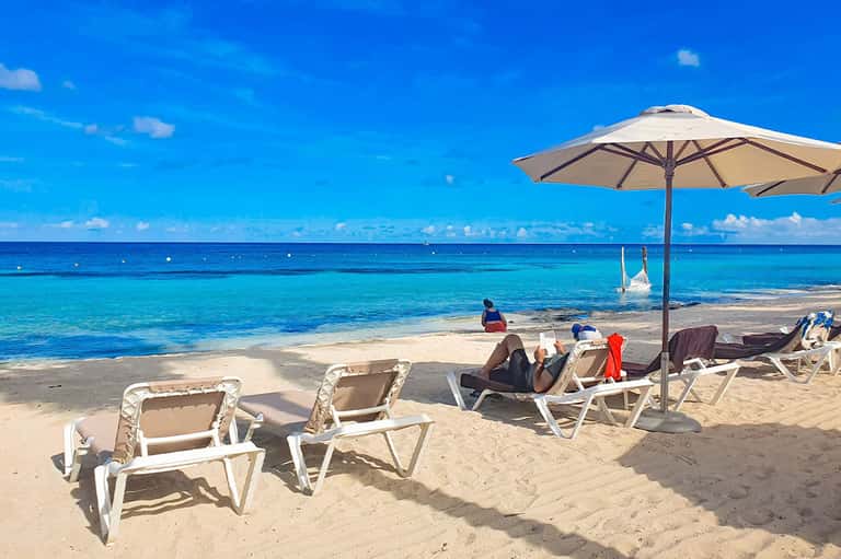 Beach lounge chairs and umbrella with crystal blue ocean water and white sand