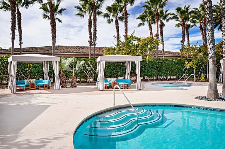Resort pool deck with cabanas and palm trees under blue sky
