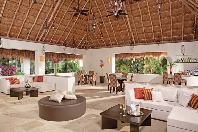 Elegant thatched-roof lounge with white furniture, tropical plants, and ocean views
