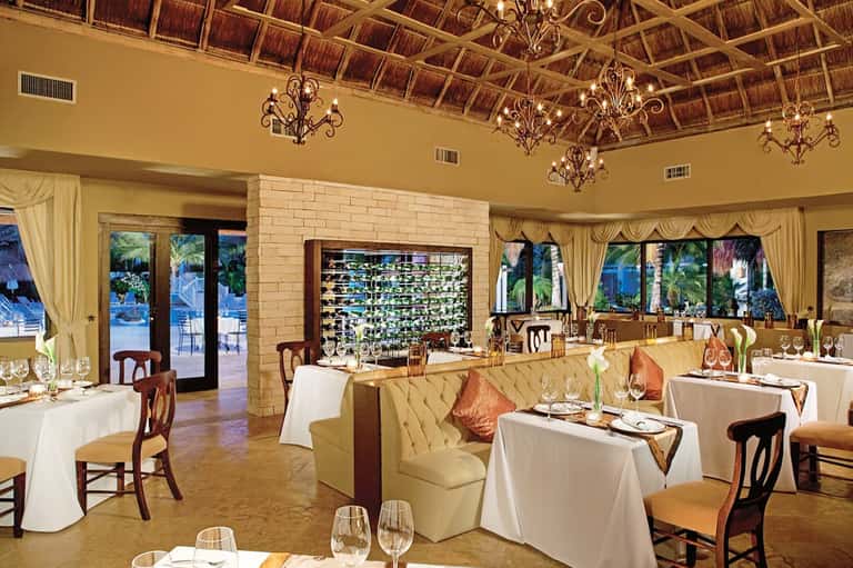 Upscale restaurant with thatched ceiling, elegant white-draped tables, and wine wall display