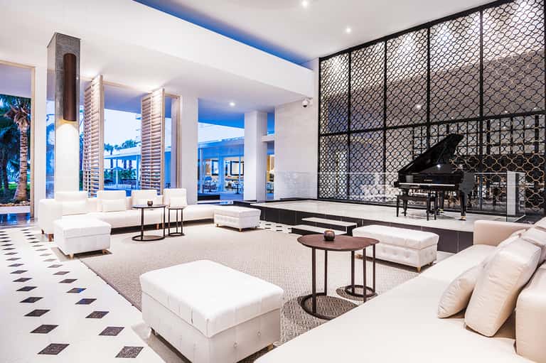 Modern hotel lobby with white seating, black fireplace screen, grand piano, and ocean view