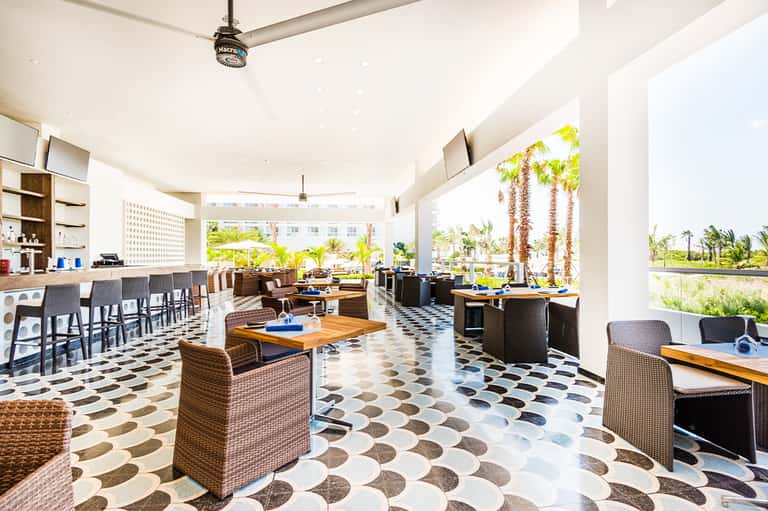 Contemporary resort restaurant with open-air covered patio, geometric flooring, and palm tree views