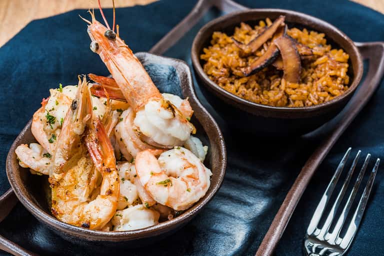 Sautéed shrimp with garnish in bowl alongside seafood paella rice dish