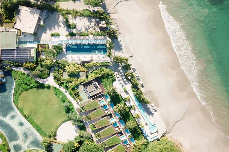 Aerial view of beachfront resort with pools, gardens, white sand beach, and ocean