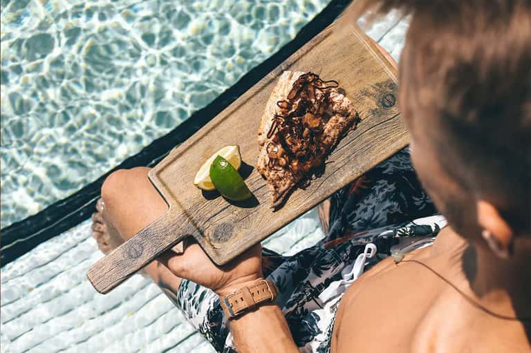 Person relaxing on overwater deck holding tray with chocolate treat and lime