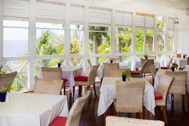 Waterfront dining room with wicker chairs, white tablecloths, and water views