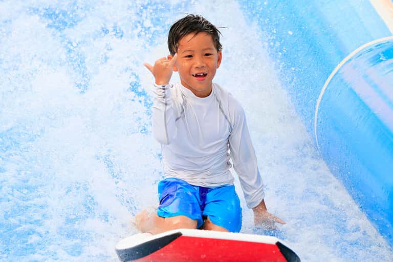 Young boy playing in water slide at resort with splashing water and blue background
