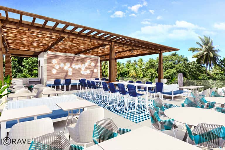 Modern outdoor lounge with wooden pergola, blue and white seating, geometric patterned rug, and tropical views