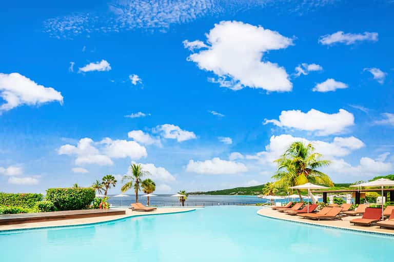 Oceanfront resort pool with lounge chairs, palm trees, and clear blue sky