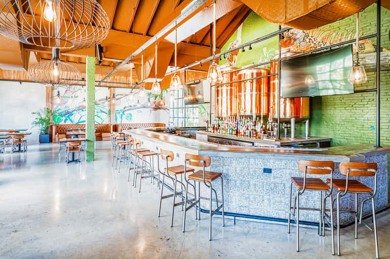 Bright bar interior with orange geometric ceiling, blue tile accents, and modern pendant lighting