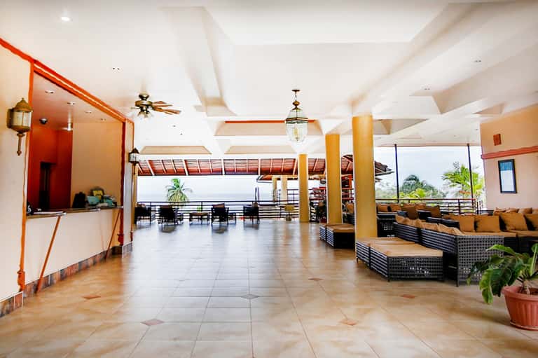 Resort lobby with terra cotta accents, white columns, ceiling fans, and ocean view balcony