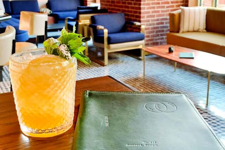 Orange cocktail with fresh mint garnish on wooden table in modern lounge