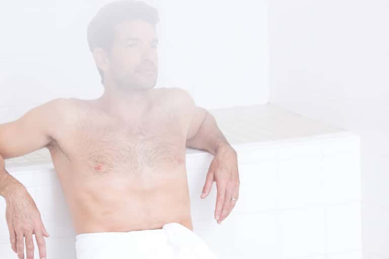Shirtless man relaxing on white chair against minimalist white background