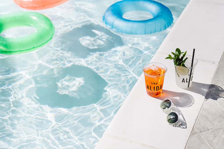Colorful pool floats on crystal clear swimming pool with drinks and sunglasses on poolside deck
