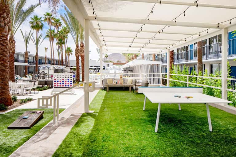 Modern resort courtyard with artificial turf, games, palm trees, and mountains in background