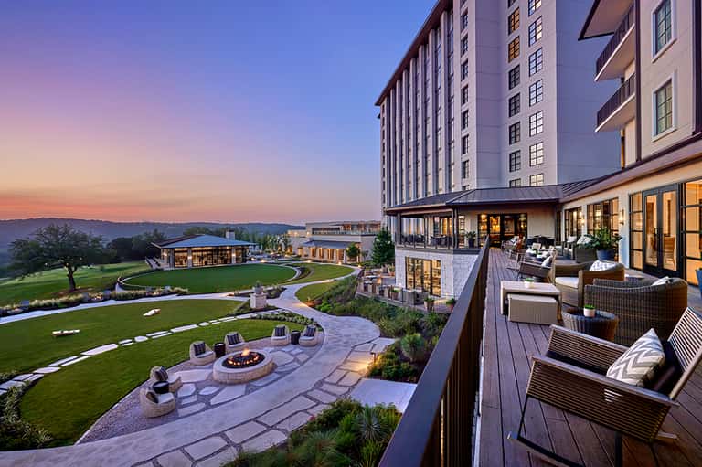 Luxury resort overlooking manicured lawns, fire pit, and mountains at dusk