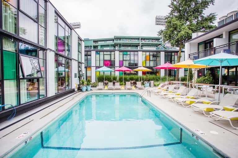 Modern outdoor pool with colorful umbrellas, lounge chairs, and contemporary hotel building with large windows