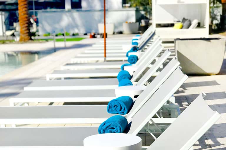 Row of white lounge chairs with blue rolled towels at a poolside resort patio