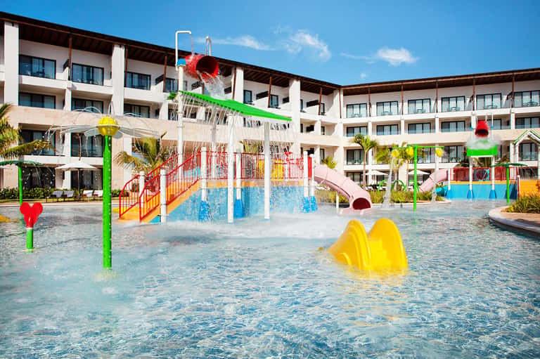 Colorful children's splash pad with water features and resort buildings in background