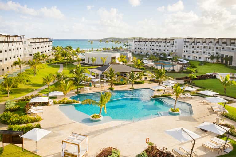Aerial view of resort pool, grounds, palm trees, ocean, and multi-story hotel buildings