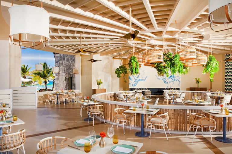 Upscale beachfront restaurant with wooden furniture, hanging plants, and ocean view