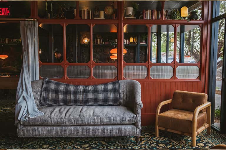 Vintage-style living room with gray patterned sofa, plaid throw, tan chair, and red-framed windows