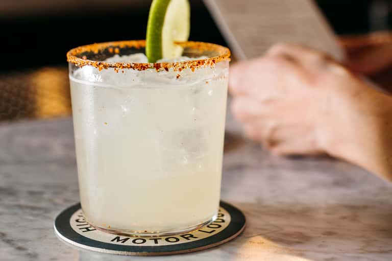 Spicy margarita with salt rim and lime wheel on dark coaster at bar