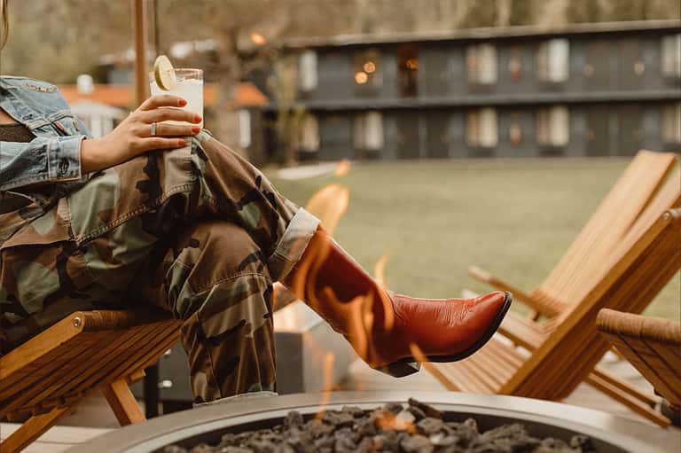 Person relaxing in wooden lounge chair holding a drink overlooking resort grounds