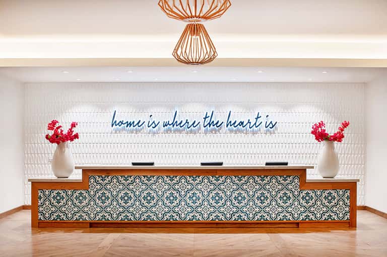 Modern hotel reception desk with blue neon sign reading 'home is where the heart is'