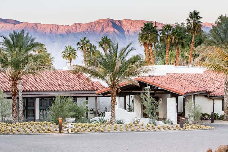 Desert resort building with terracotta roof, palm trees, and mountains in background