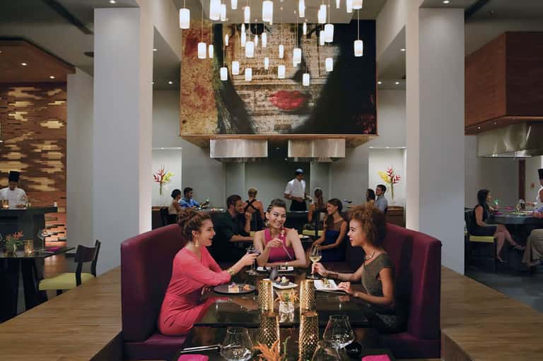 Modern hotel lobby with burgundy seating, pendant lighting, and guests dining and socializing