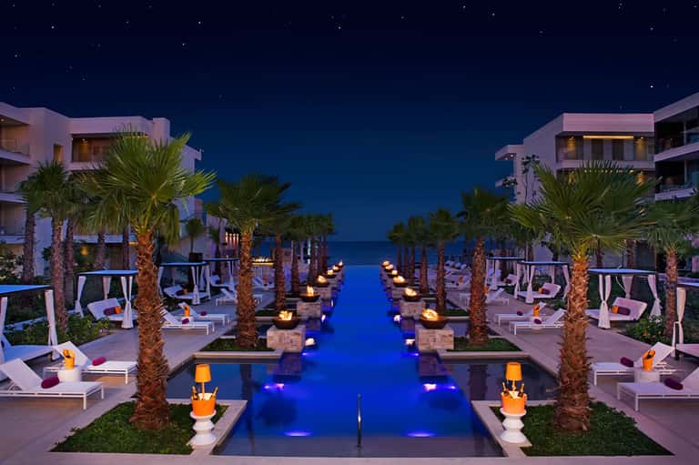 Luxury beachfront resort with infinity pool, palm trees, and ocean view at night