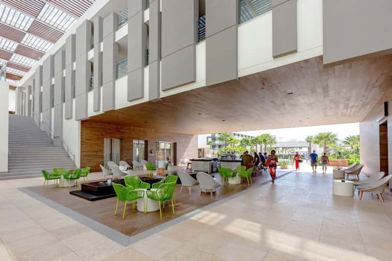 Modern resort lobby with bright natural lighting, green chairs, wooden accents, and open architectural design