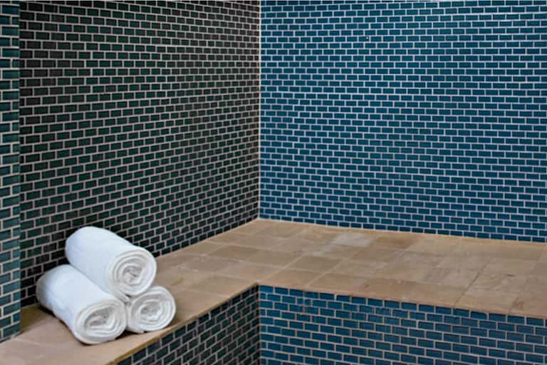 Spa shower area with teal brick walls, stone bench, and rolled white towels