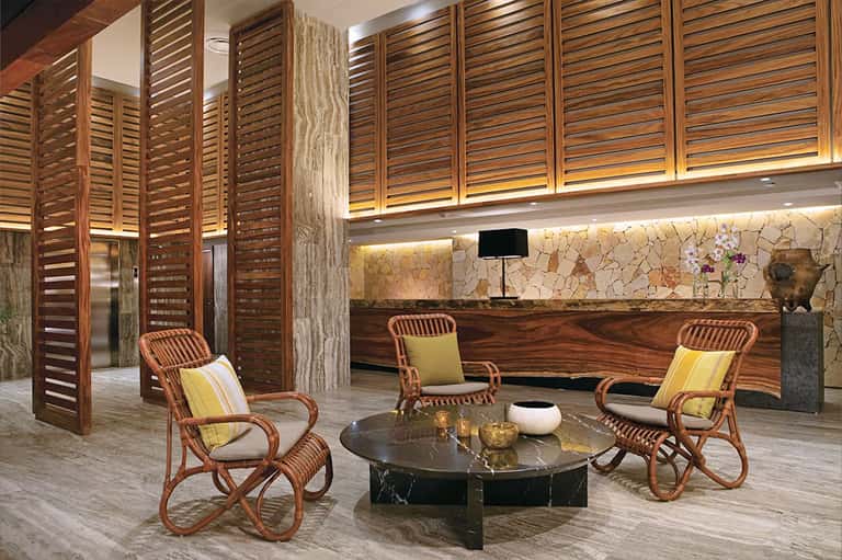 Luxury lobby lounge with wooden shutters, rattan chairs, and black marble table