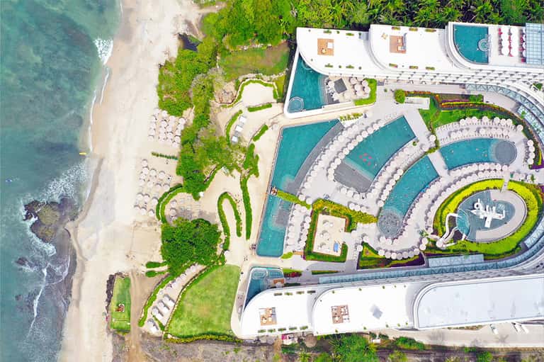 Aerial view of resort pools and white loungers on sandy beach with turquoise ocean