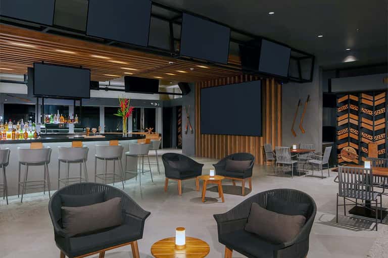Contemporary lounge with bar, wood accents, dark seating, and entertainment screens