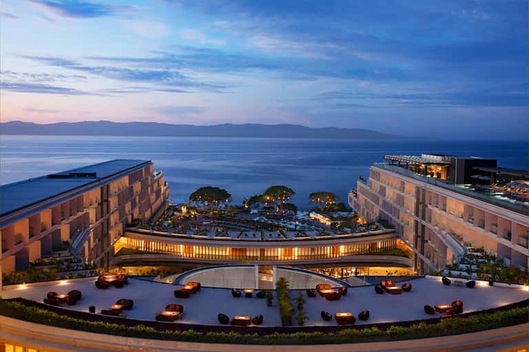 Luxury resort terrace at dusk with fire bowls, curved architectural elements, ocean and mountain views