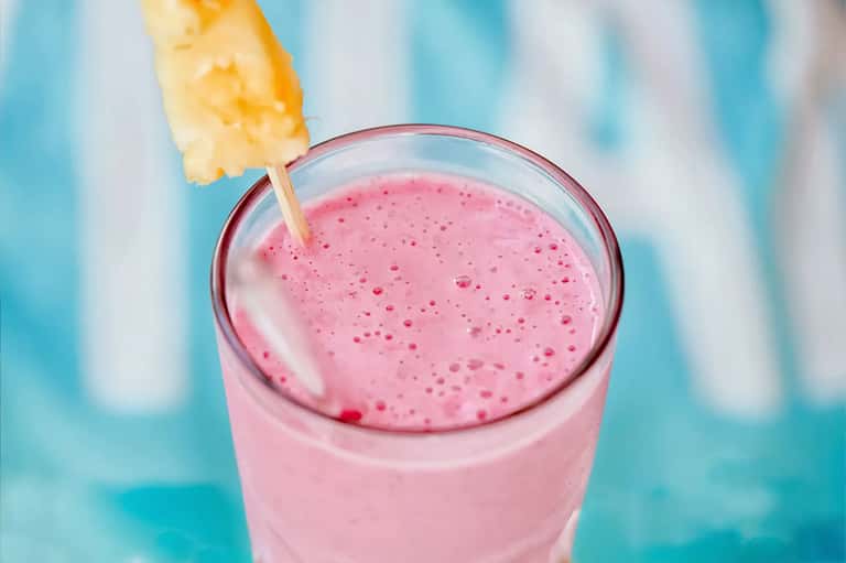Pink smoothie or açai bowl with pineapple garnish against turquoise background