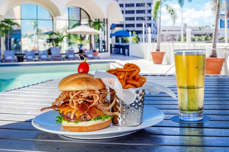 Gourmet burger with fries and beverage on poolside dining table with arched architecture