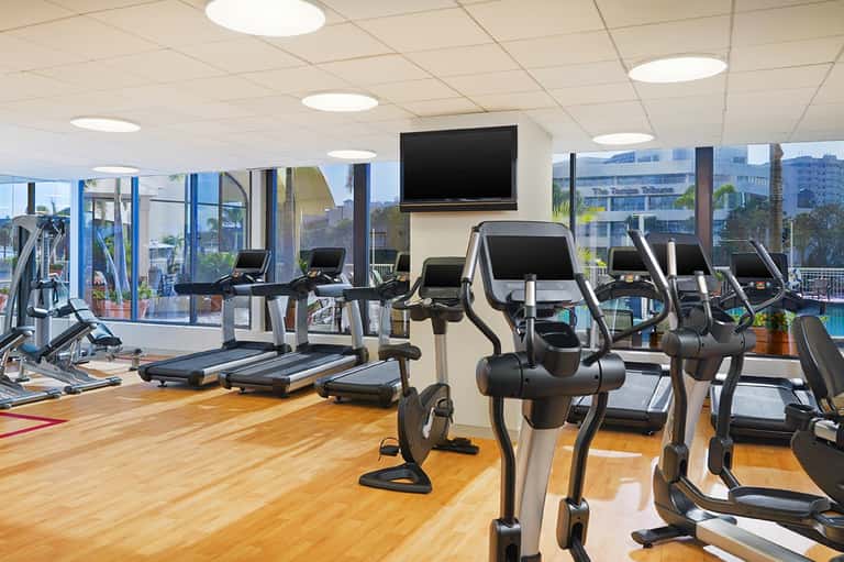 Modern fitness center with exercise bikes and treadmills overlooking a pool through large windows