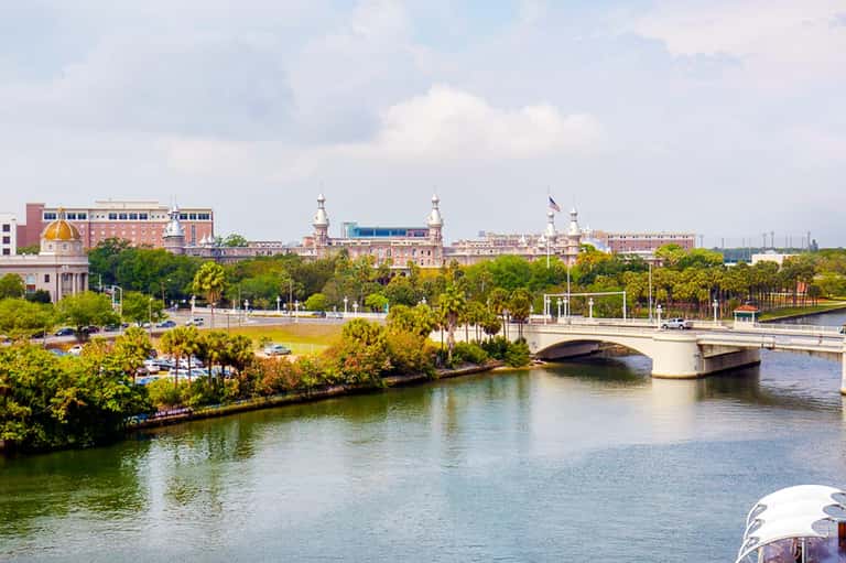 Aerial view of riverside cityscape with historic buildings, bridges, palm-lined waterfront and green spaces