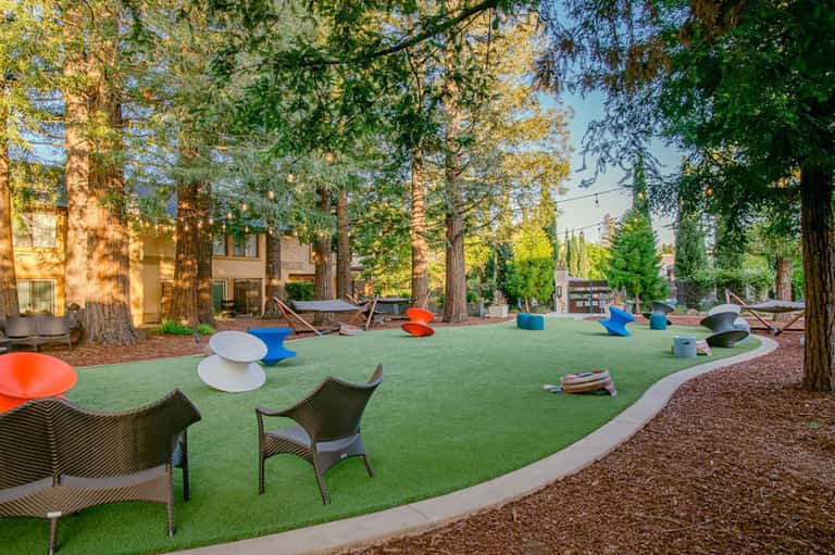 Modern resort courtyard with green synthetic turf, large trees, and colorful art sculptures