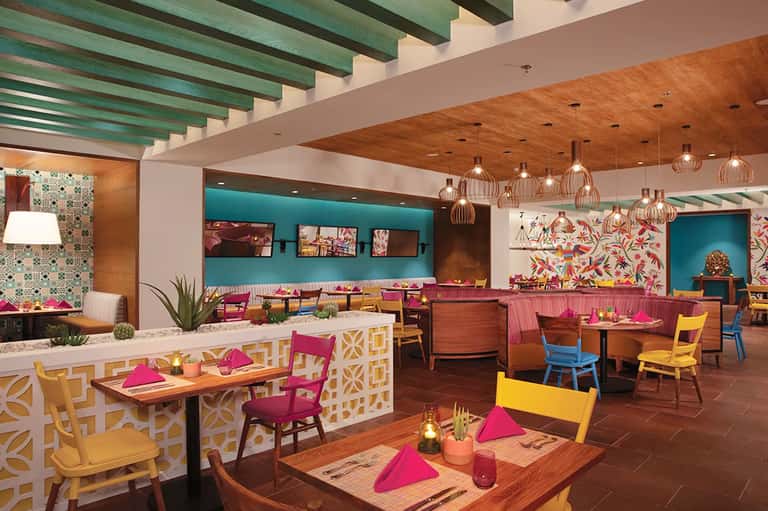 Colorful modern restaurant interior with turquoise walls, wooden beams, pink furniture and geometric patterns