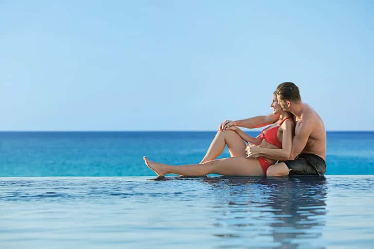Couple relaxing in infinity pool overlooking turquoise ocean water
