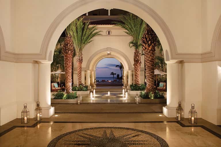 Elegant archway with palm trees leading to illuminated oceanfront promenade at dusk
