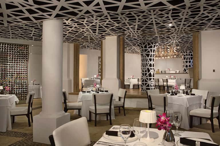 Upscale restaurant dining room with geometric patterned ceiling, white tablecloths, and elegant table settings