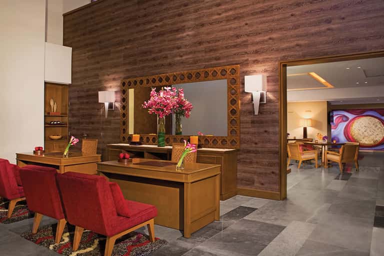 Hotel lobby with wood-paneled walls, decorative mirror, fresh flowers, and modern furnishings